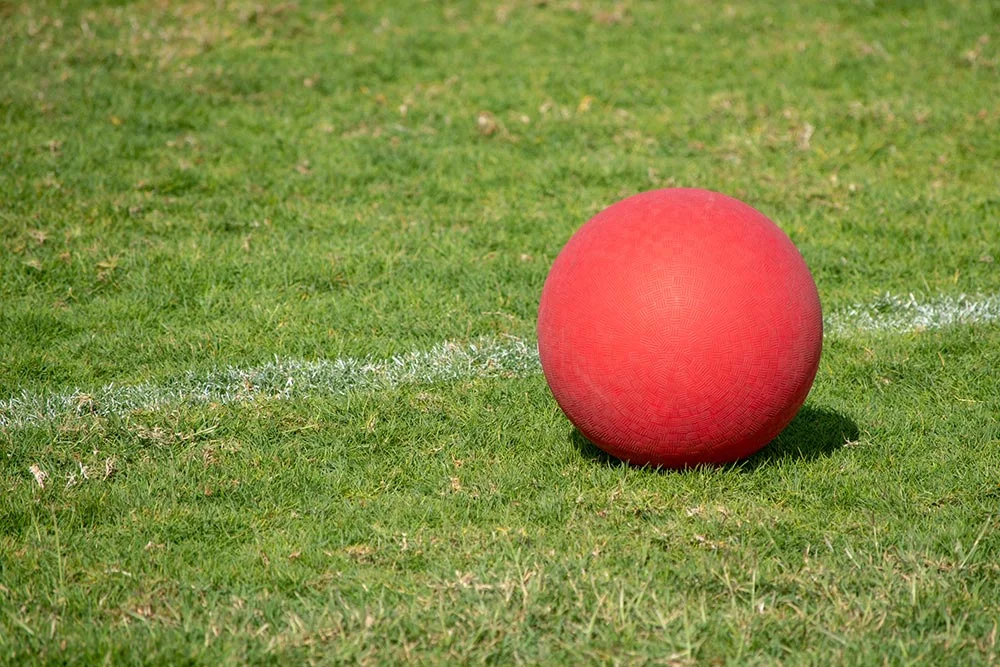 A red rubber ball on a playground field. Playground ball game rules concept.